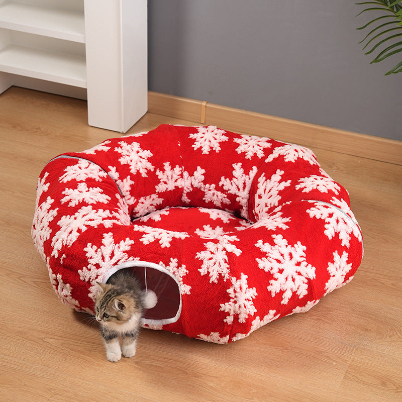 Red and white patterned pet bed with a cat peeking out on a wooden floor.