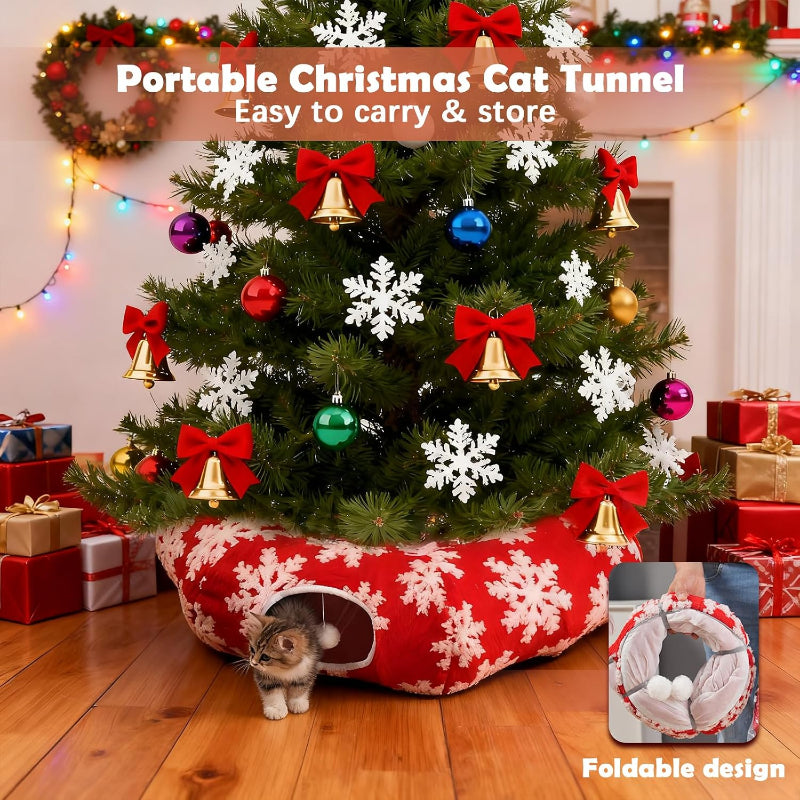 A small cat stands in a red and white snowflake-patterned portable cat tunnel placed at the base of a decorated Christmas tree in a living room. The scene includes holiday ornaments, wrapped gifts, string lights, and text overlays reading 'Portable Christmas Cat Tunnel' and 'Foldable design.