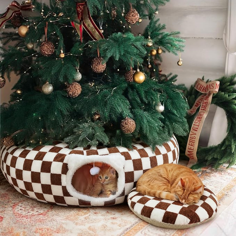 Two cats resting on checkered pet beds in front of a decorated Christmas tree.